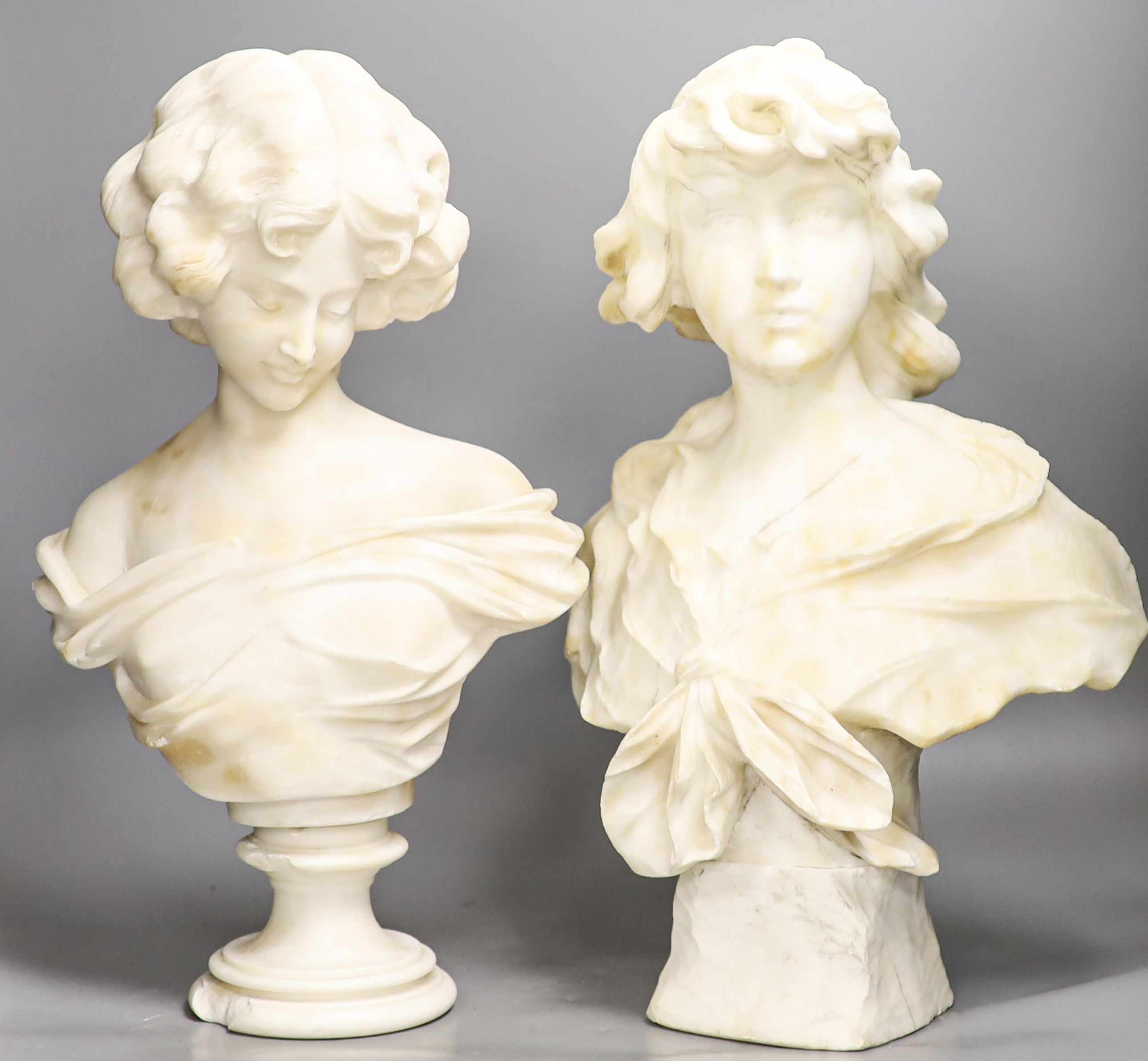 Two white alabaster busts of young women, raised on turned plinths 44cm